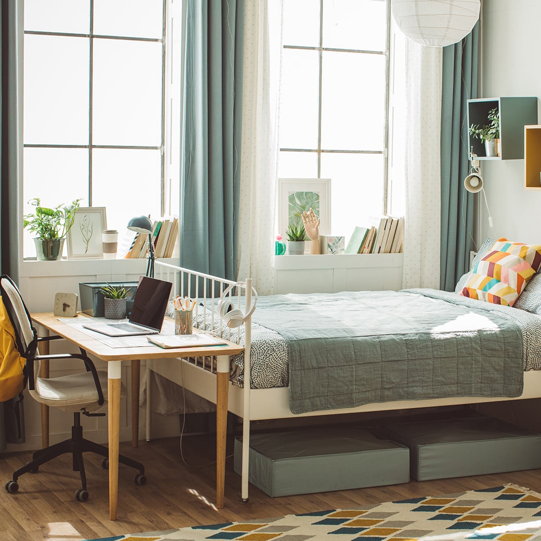 Bright student accommodation bedroom featuring a bed, study desk with laptop, and large windows letting in natural light. 