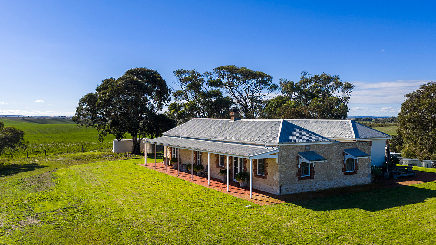 Elevated view of a restored stone farmhouse surrounded by open grassland, mature trees, and rolling agricultural fields. 