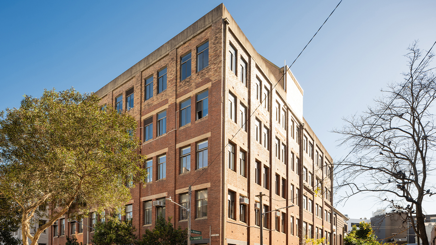 A contemporary mid-rise residential apartment building with a warm brick façade, large windows and leafy street frontage, situated within an established urban neighbourhood. 