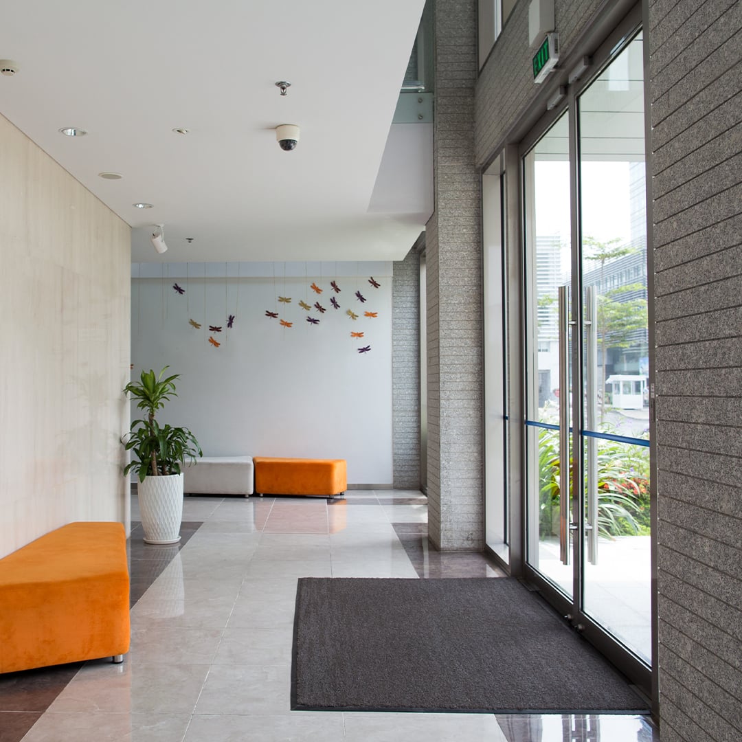 Modern building lobby with orange bench seating, a potted plant, decorative wall art, and floor-to-ceiling glass doors letting in natural light. 