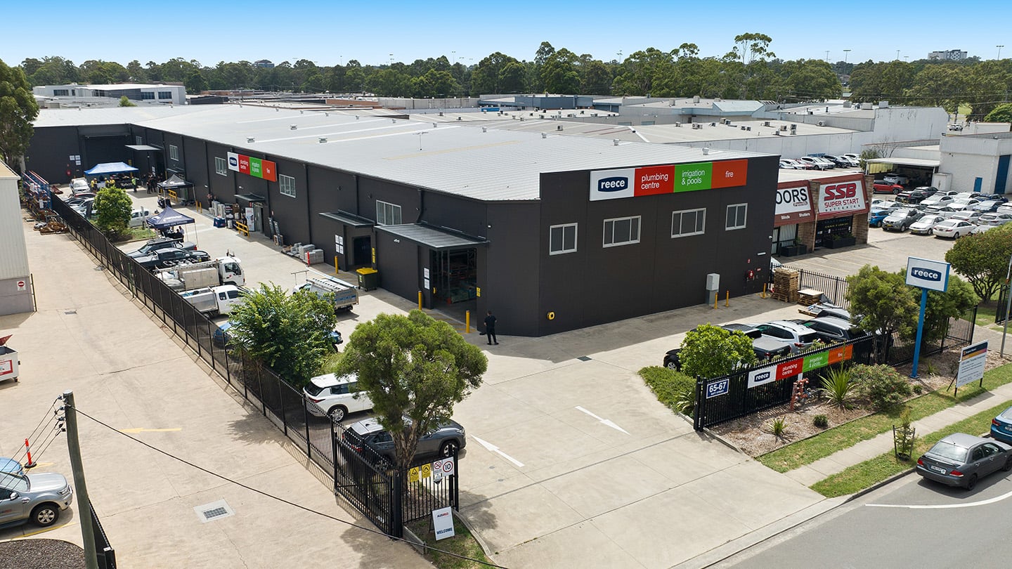 Aerial view of a large Reece industrial and showroom facility with branded signage, parking areas, delivery vehicles, and surrounding buildings in a business precinct. 