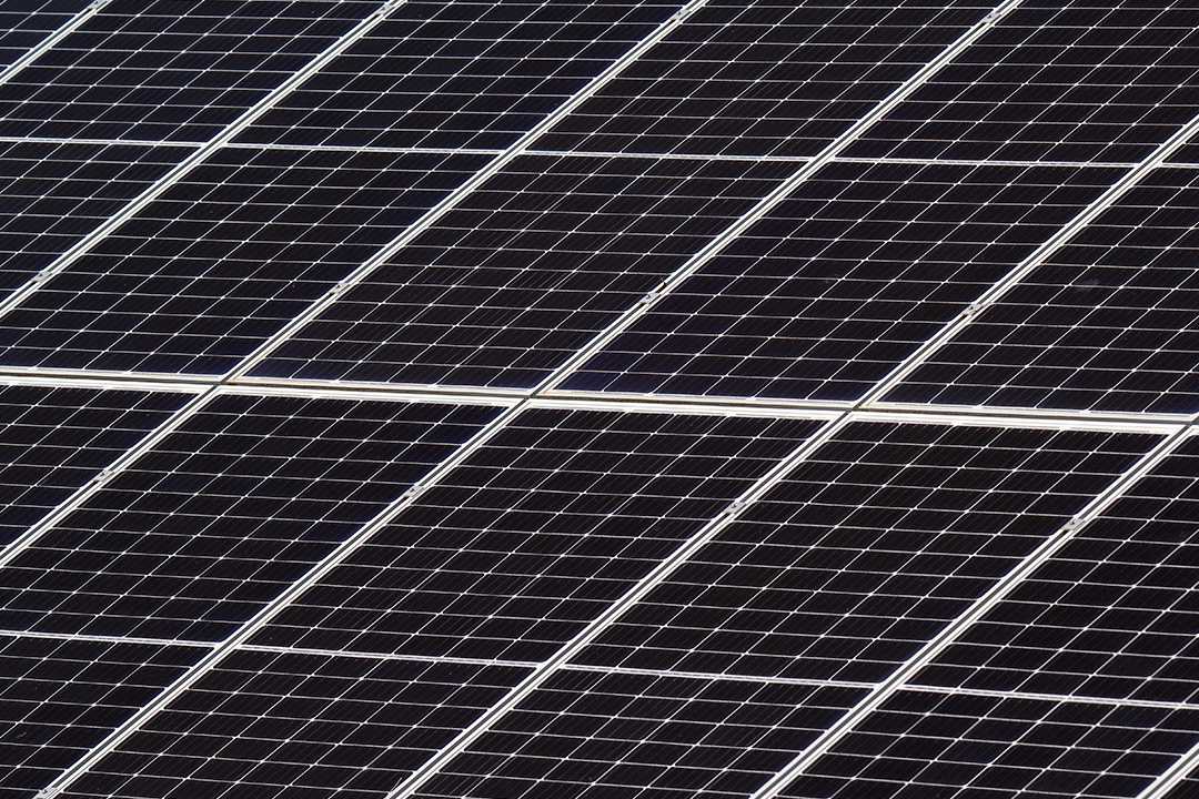 A close-up, high-angle shot reveals a grid of black solar panels, each sectioned into smaller squares by thin white lines, all arranged diagonally across the frame.