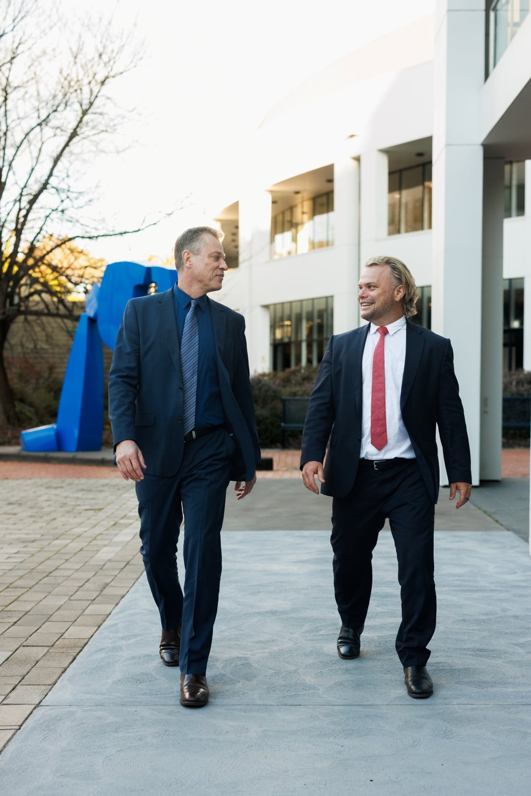 Todd Svanberg & Ty Noble walk and chat together outside a modern office building.