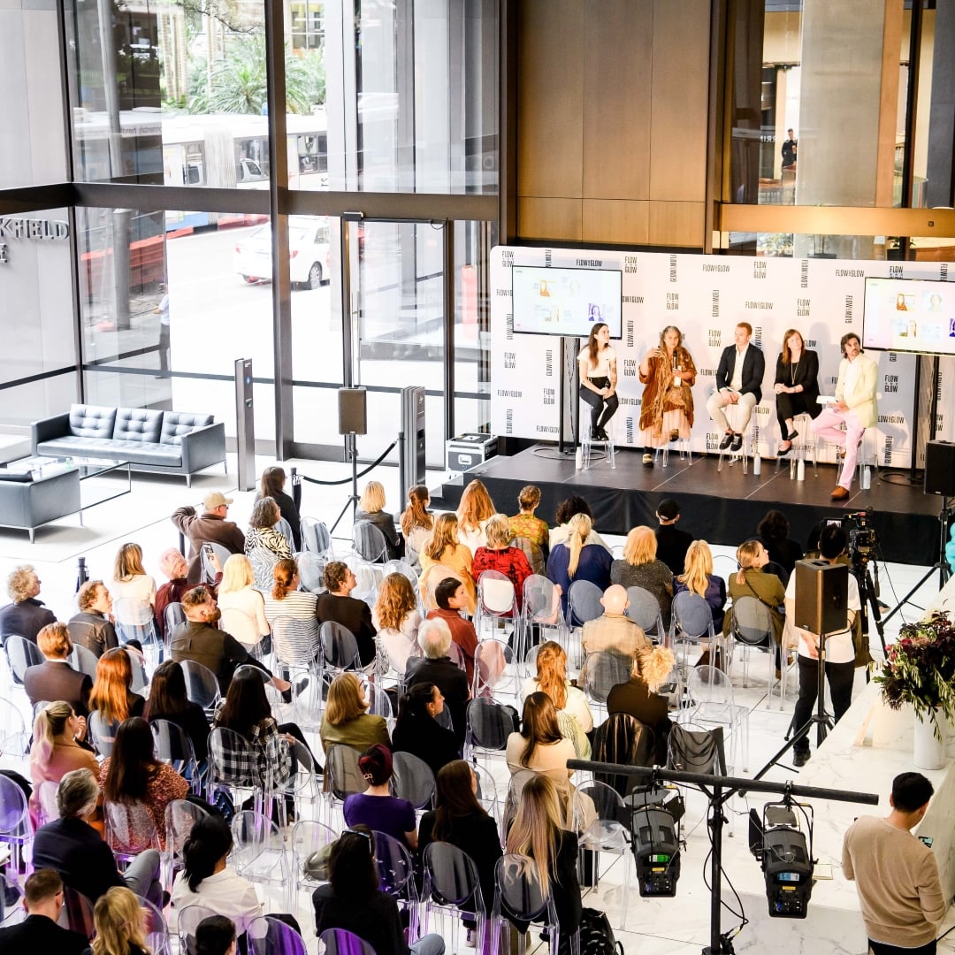 A panel of five speakers sits on a stage before an audience at a 