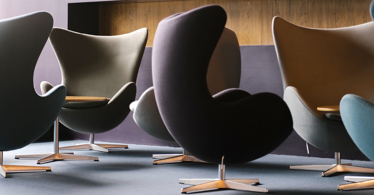 Modern curved chairs in various colors arranged in a semi-circle on a carpeted floor with wood-paneled walls.