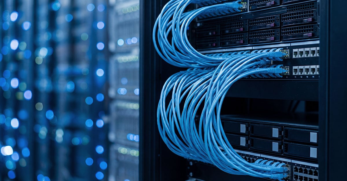 Close-up of bundled blue ethernet patch cables looping between black server racks in a commercial data center facility.