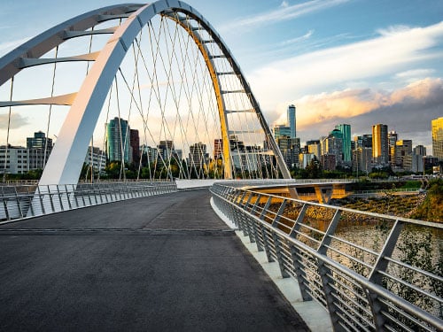 Walterdale Bridge pedestrian path in Edmonton Alberta with the downtown office and commercial real estate skyline visible in the background at dusk.
