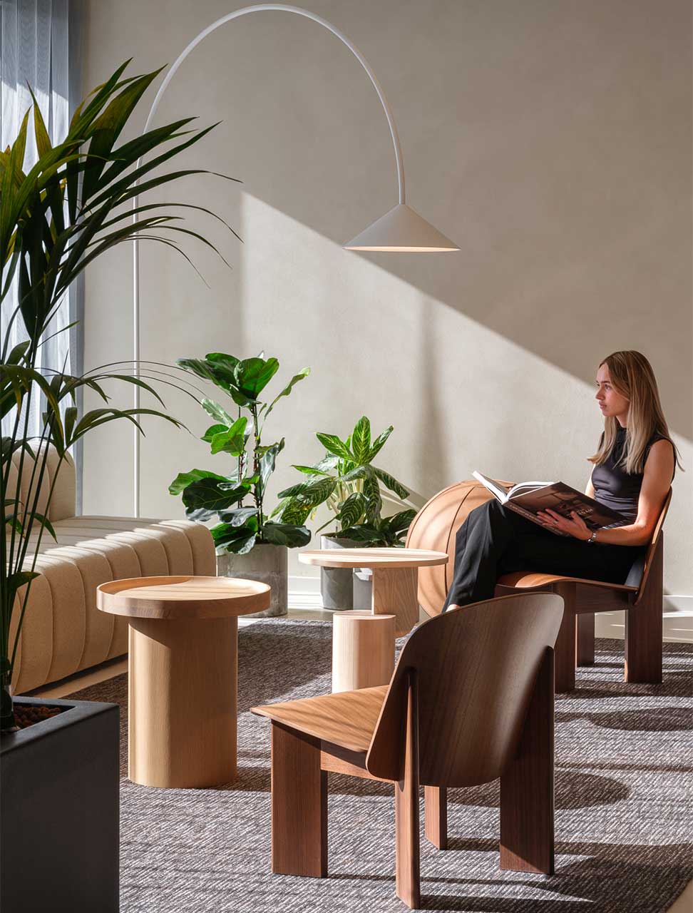 A lady with a book on her lap, sitting in a naturally lit sitting area, reading.