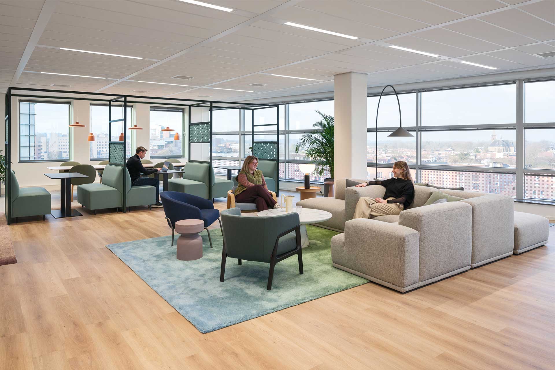 Modern office lounge with comfortable seating areas, work booths, large windows and a light, open interior.