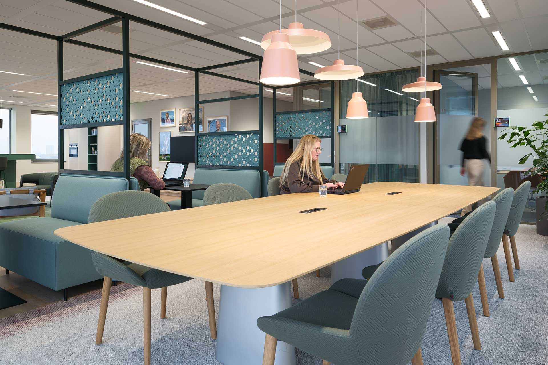 Modern office space with large wooden conference table, designer pendant lamps, workstations and comfortable upholstered chairs.