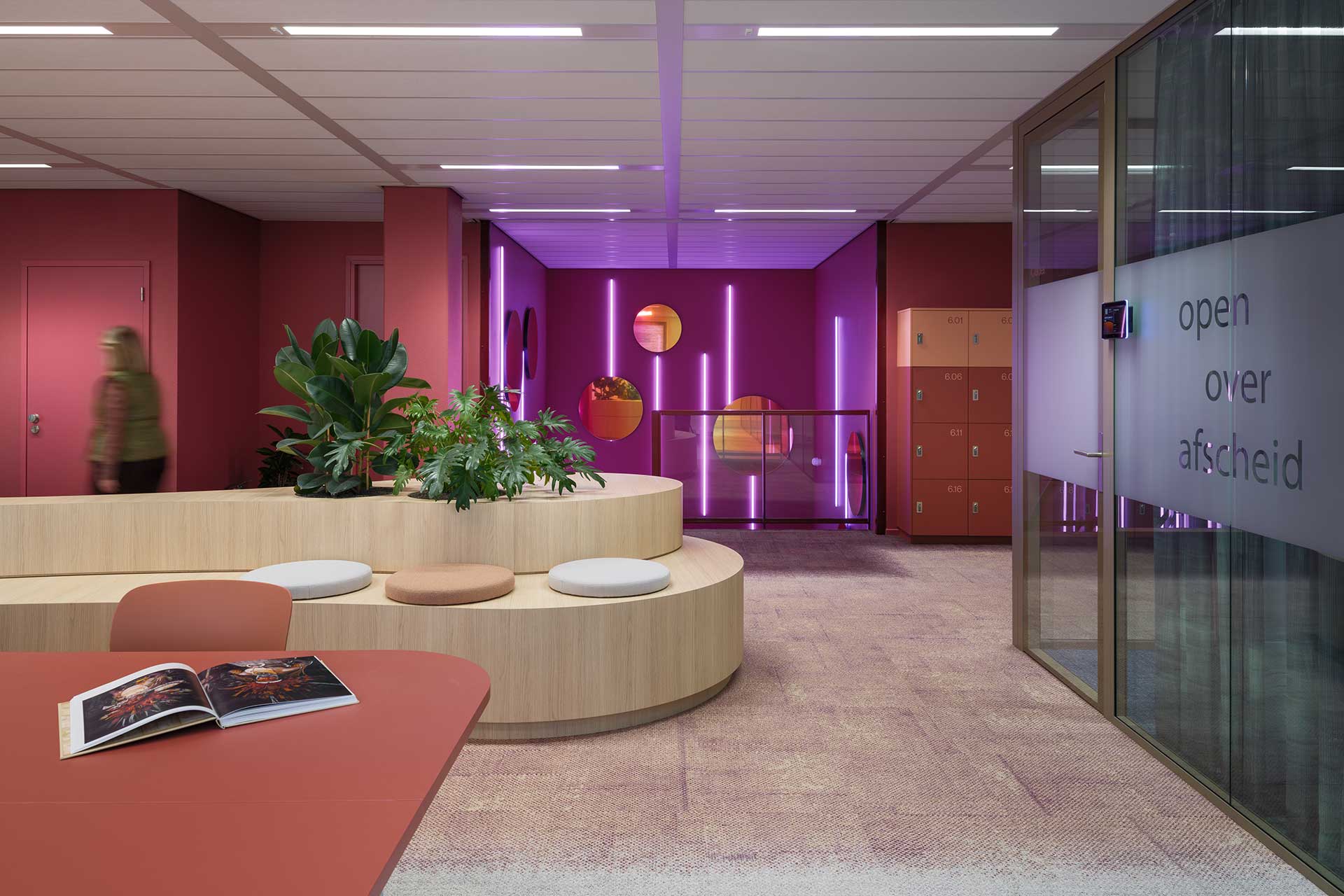 Modern office space with undulating wooden seating element, green plants, colourful LED accent wall and glass meeting room.