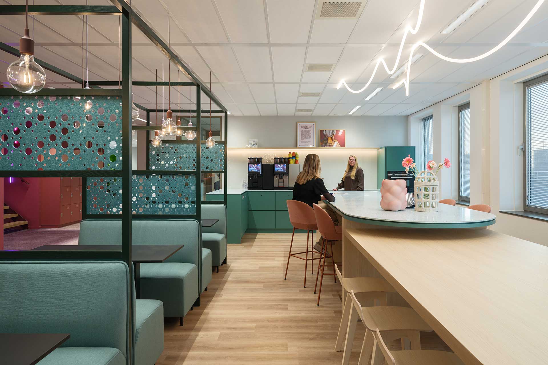 Modern office pantry with seating areas, large round table, coffee corner and decorative room dividers in shades of green.