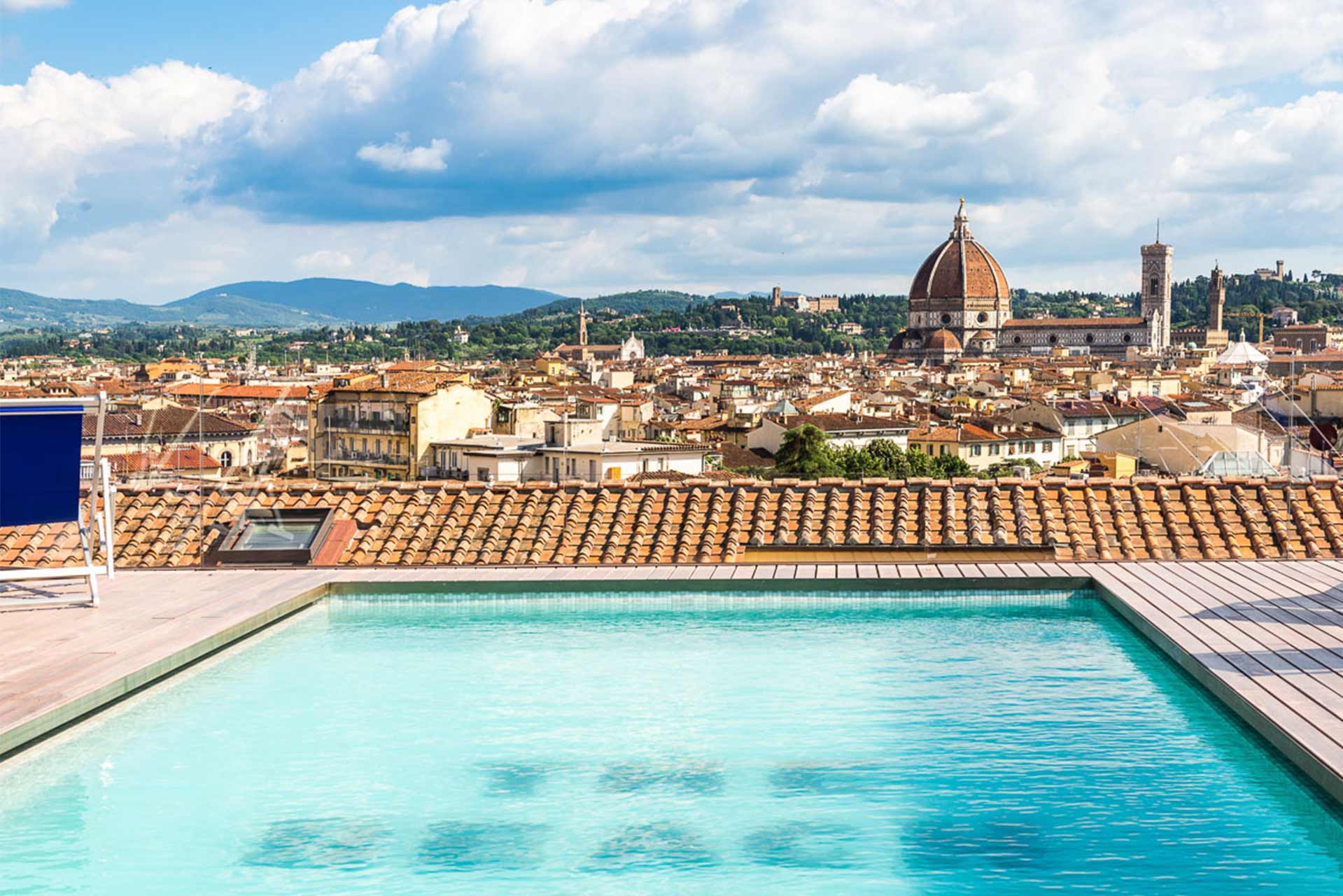 Rooftop swimming pool with panoramic view of Florence, featuring the Duomo dome and Giotto’s Campanile, under a partly cloudy sky.