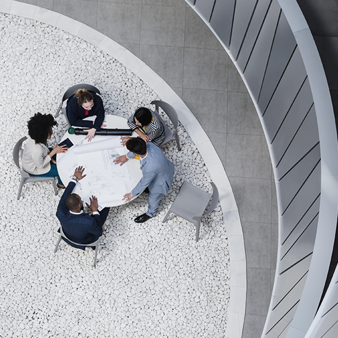 Overhead view of a diverse team of business professionals collaborating around a table, reviewing architectural plans in a modern commercial office setting.