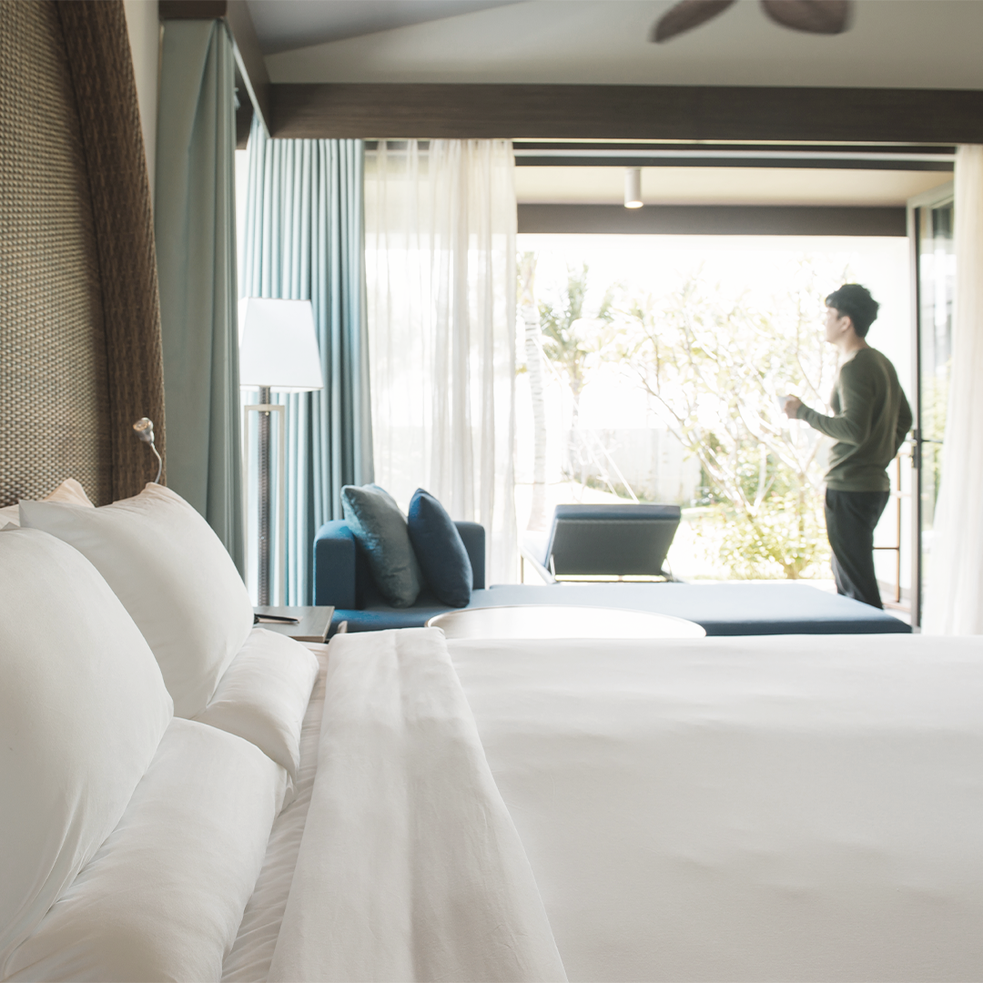 Image of a luxury hotel room with a comfortable bed, seating area, and patio view. Suggests high-end amenities and design.