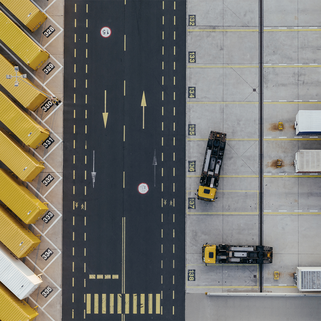 Aerial view of a commercial distribution center with yellow shipping containers and trucks parked in numbered spaces.