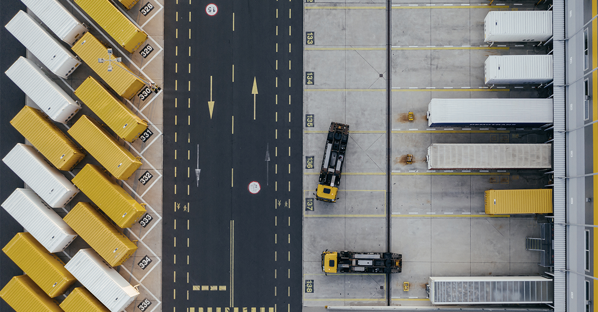 Aerial view of a commercial distribution center with yellow shipping containers and trucks parked in numbered spaces.