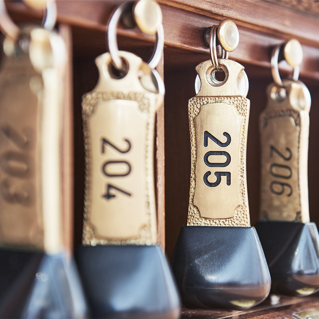 Brass hotel room keys on a wooden rack, numbers 203 through 206 visible.