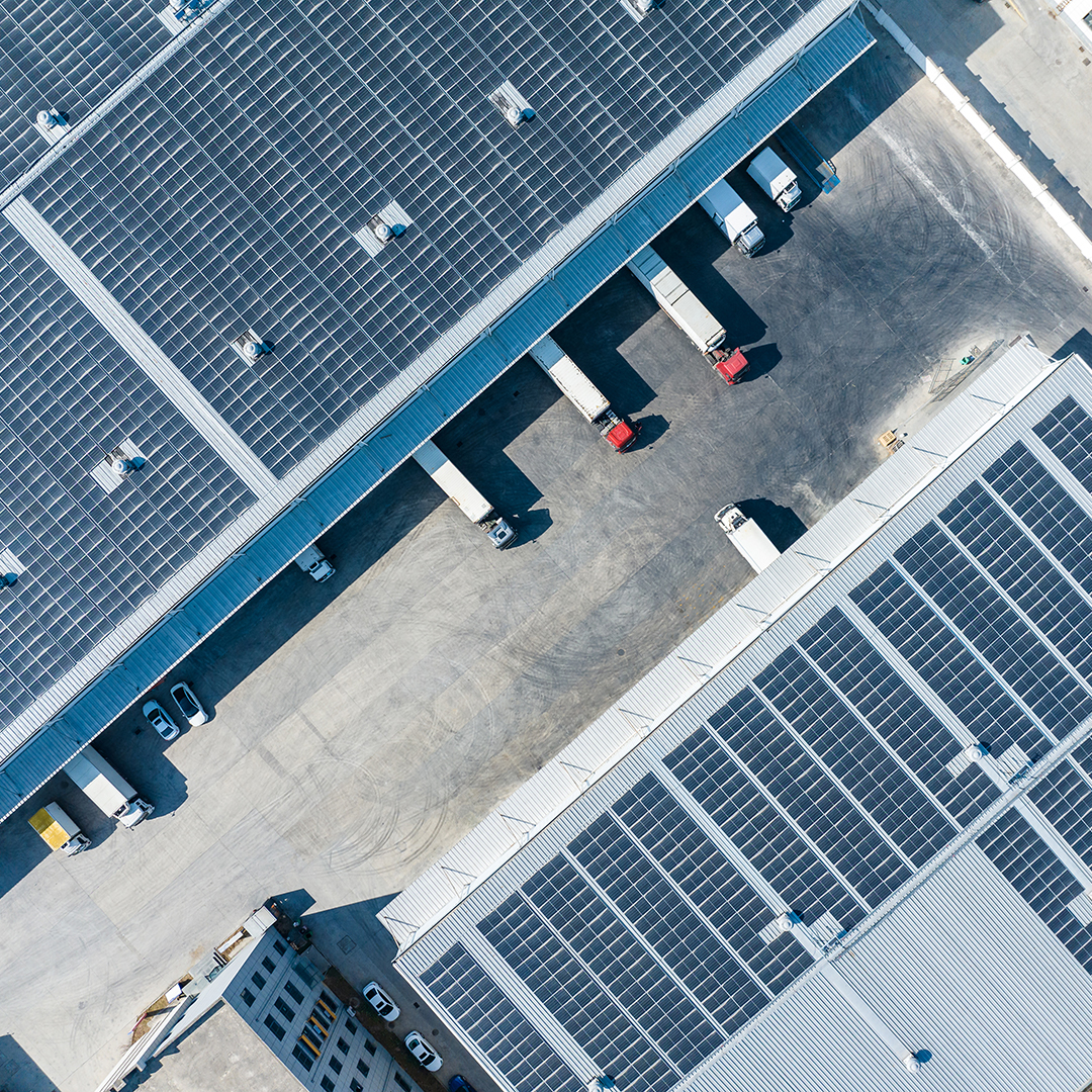 Aerial view of an industrial warehouse with solar panels covering the roof and trucks docked at loading bays
