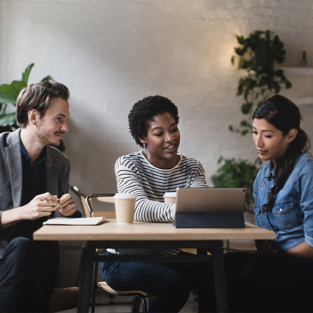 Three diverse professionals, two women and one man, collaborating around a wooden table with a tablet, discussing commercial real estate opportunities.