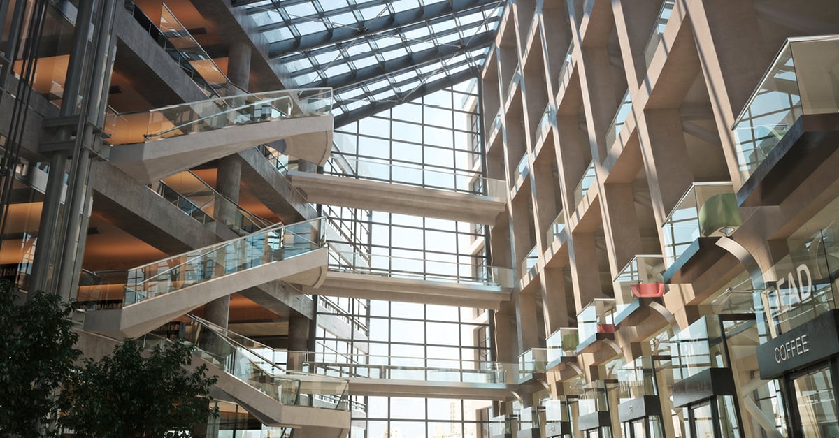 Interior of a modern building with multiple floors, angled glass walkways, and a glass ceiling allowing natural light.