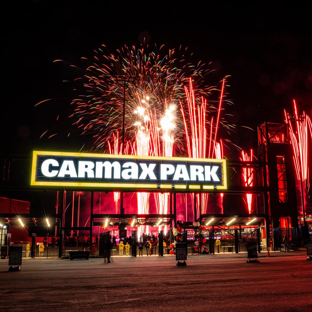 Fireworks exploding over the illuminated CarMax Park stadium entrance at night