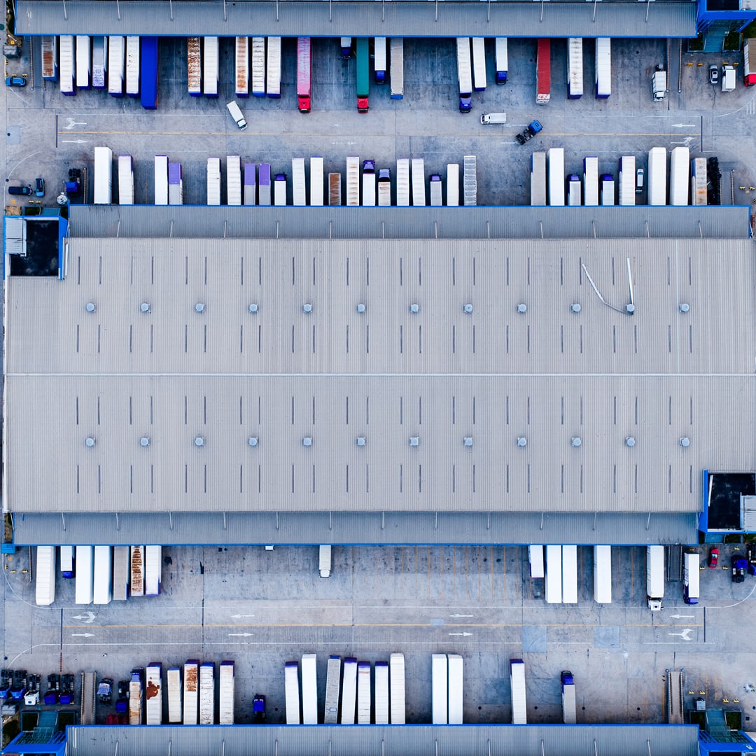 Aerial top-down view of a large logistics warehouse with rows of trucks and trailers parked at loading docks