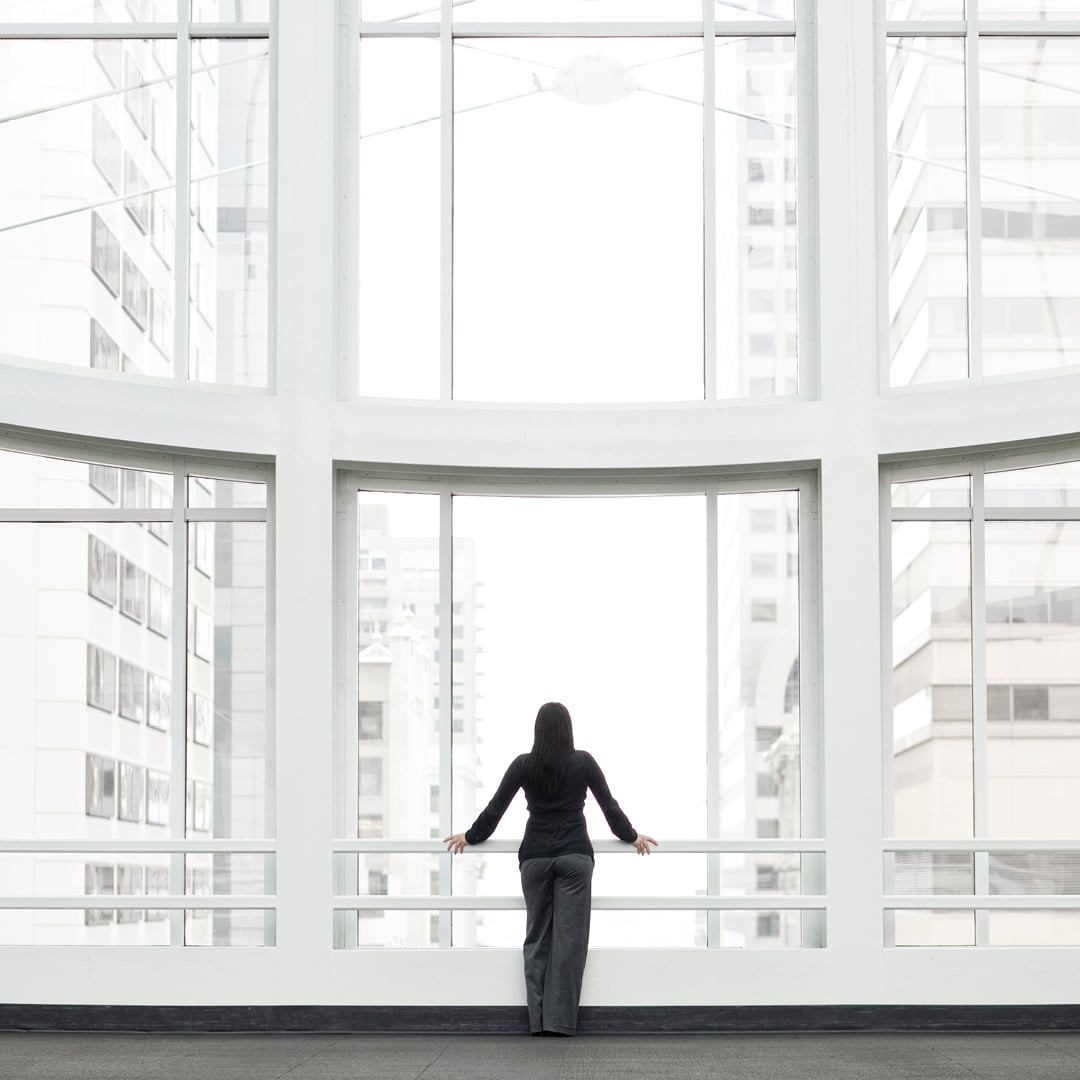 Rear view of a businesswoman standing at a large curved floor-to-ceiling window in a modern office building