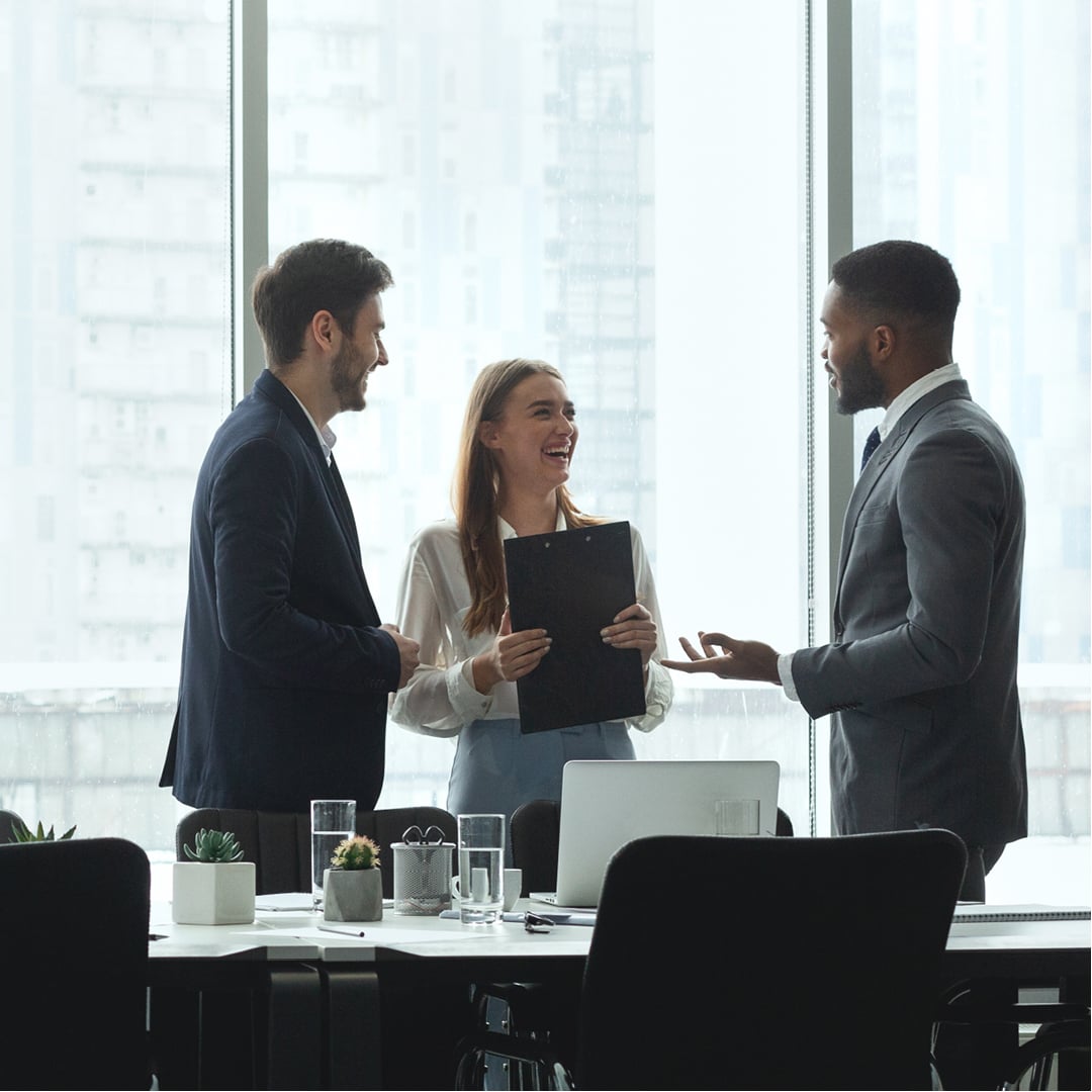 Three business professionals laughing and conversing around a conference table in a modern boardroom