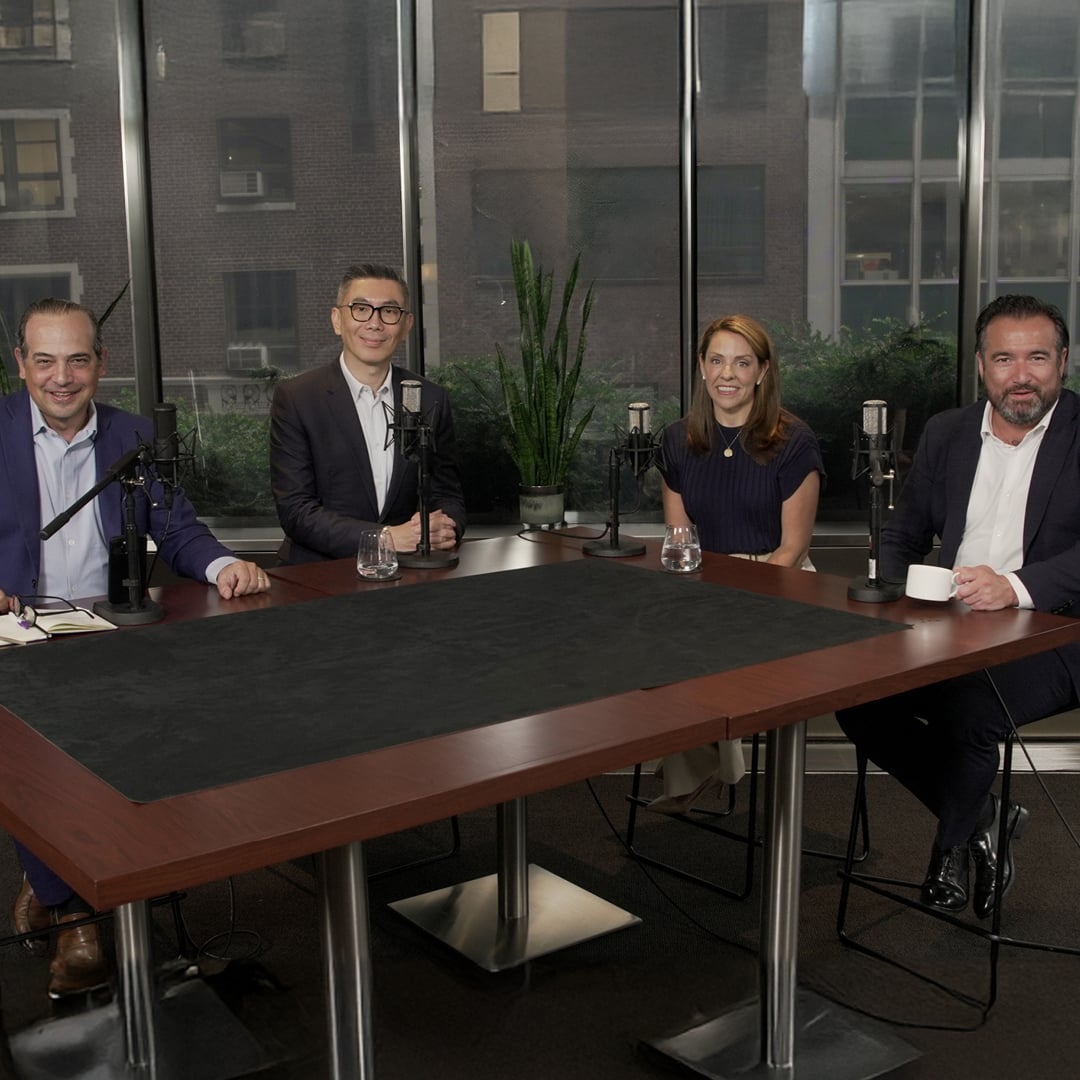 Four business professionals seated around a table with studio microphones in a podcast or panel recording setup