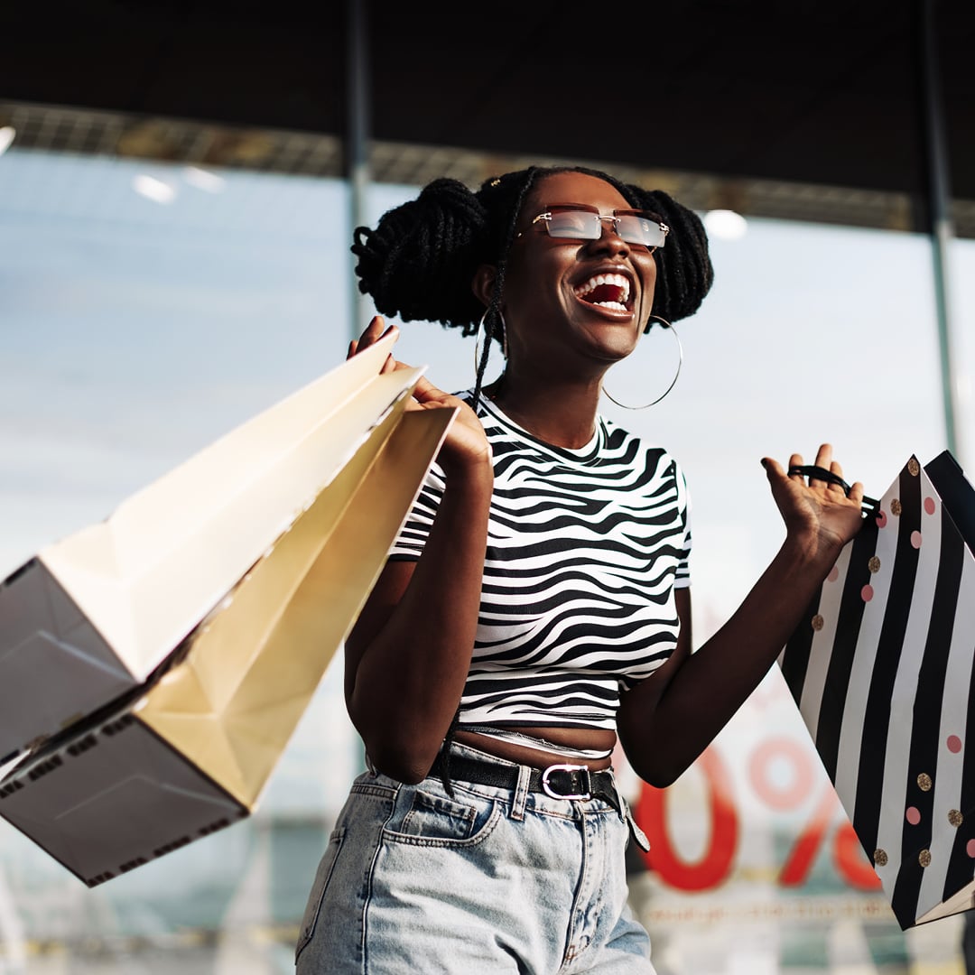 Woman laughing while carrying shopping bags outside a retail center, illustrating CBRE's The Weekly Take episode on Southeast retail investment and mixed-use development.