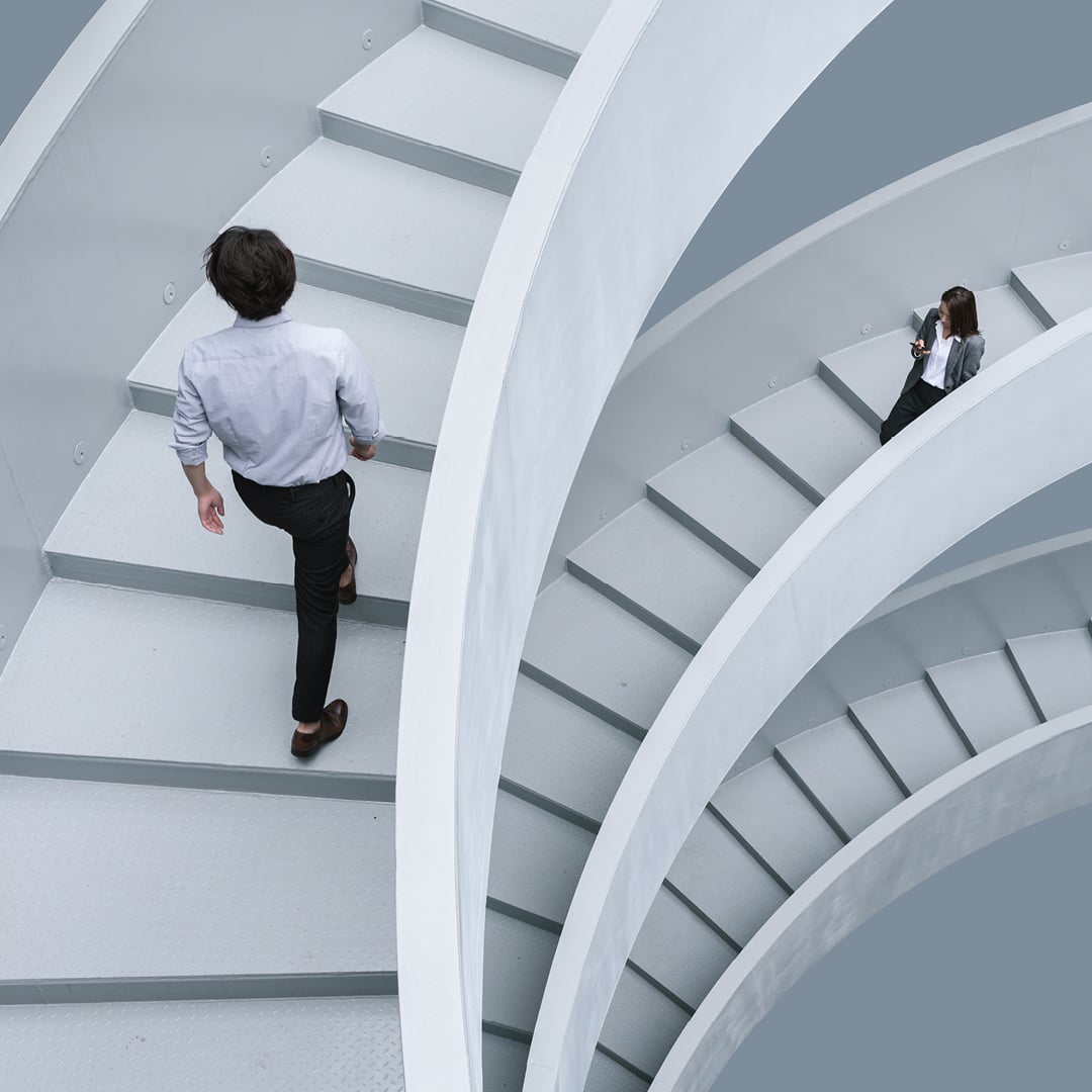Two people walk on a modern white spiral staircase viewed from above