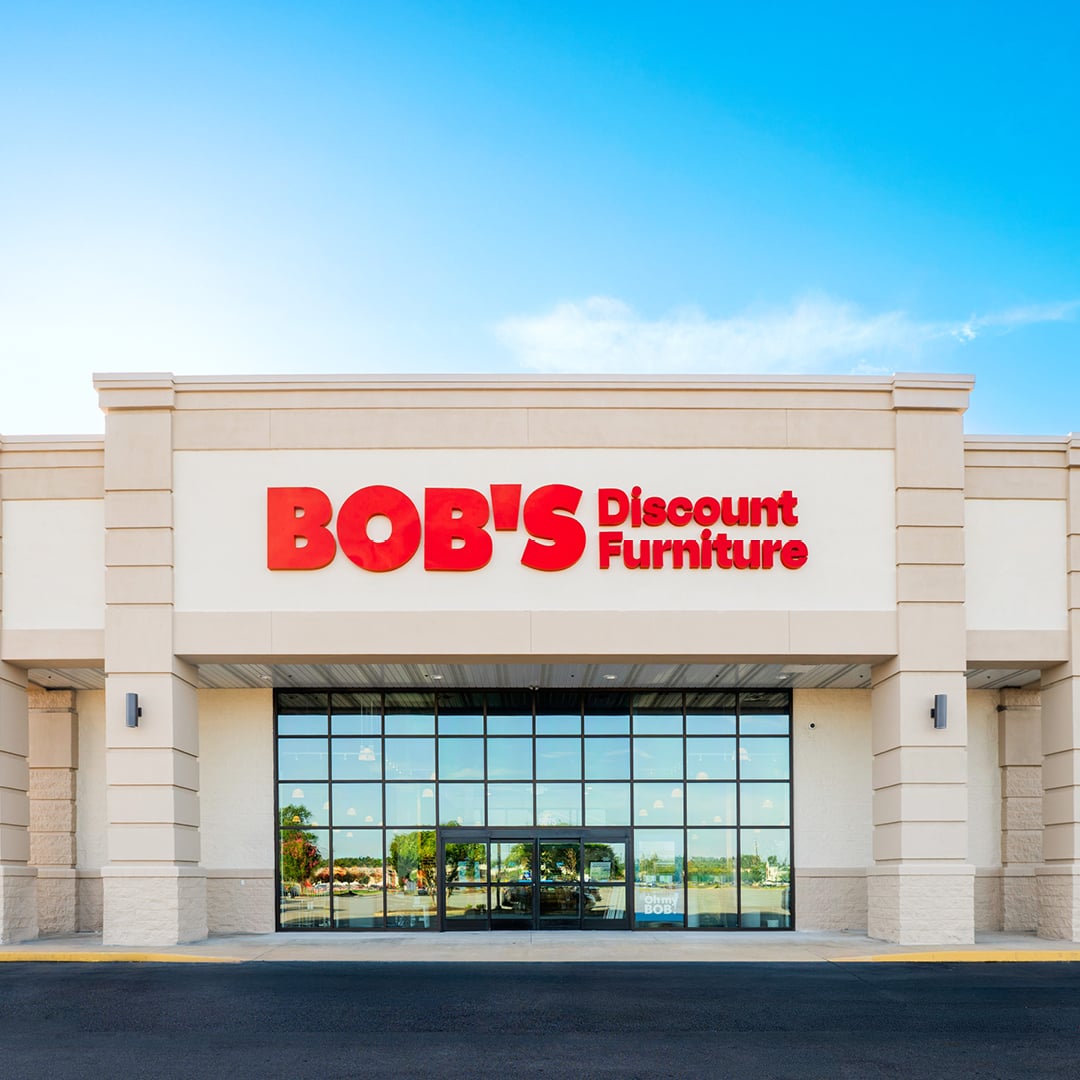 Exterior of a Bob’s Discount Furniture store with red signage and a glass entrance under blue sky