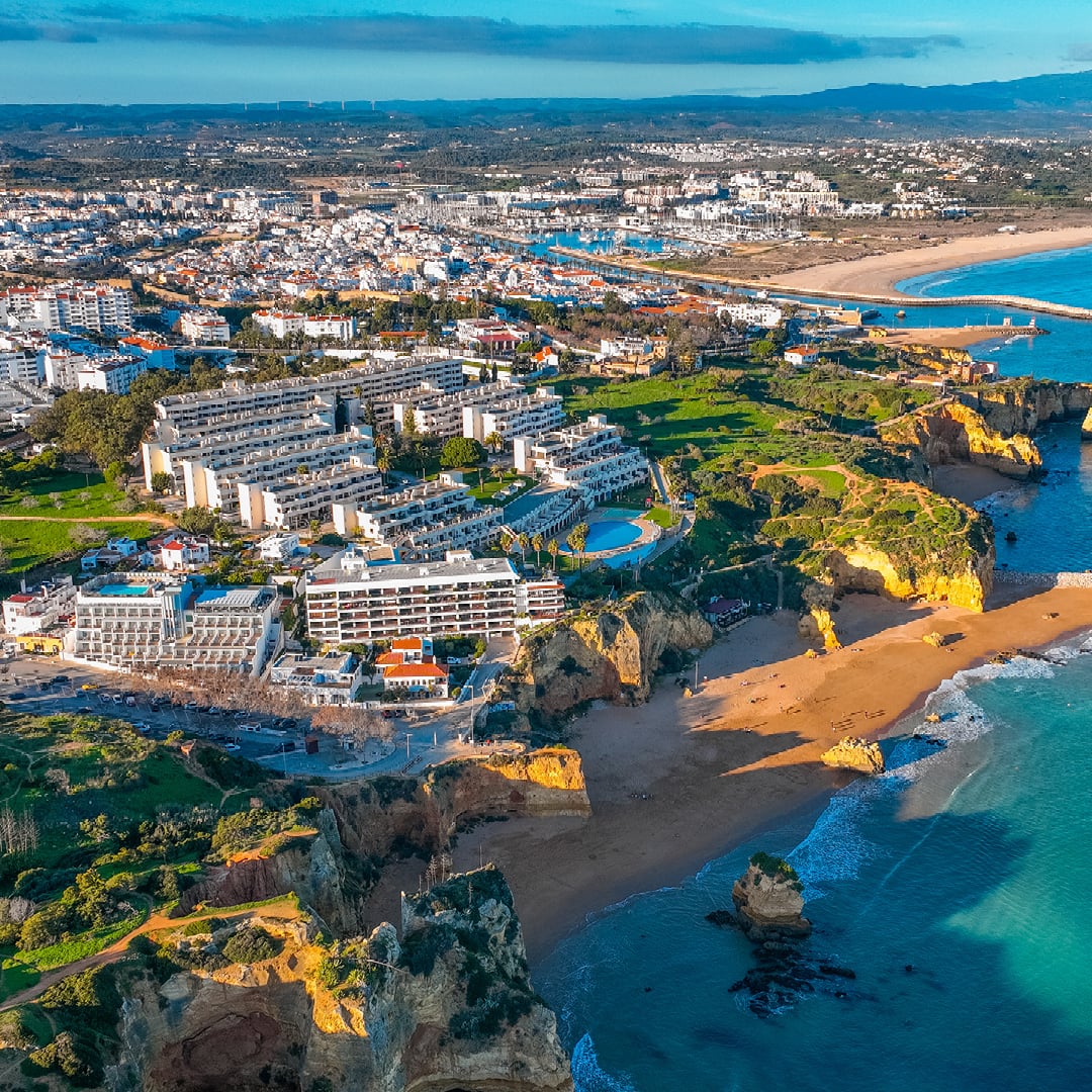 Aerial view of a coastal city with white buildings, rugged cliffs, sandy beaches and turquoise water