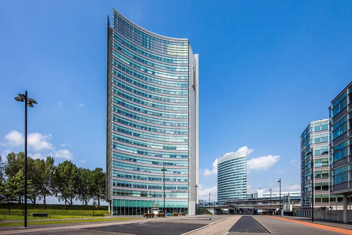 Een modern en duurzaam kantoorgebouw met meerdere verdiepingen, omgeven door groene gebieden, paden en parkeerplaatsen.