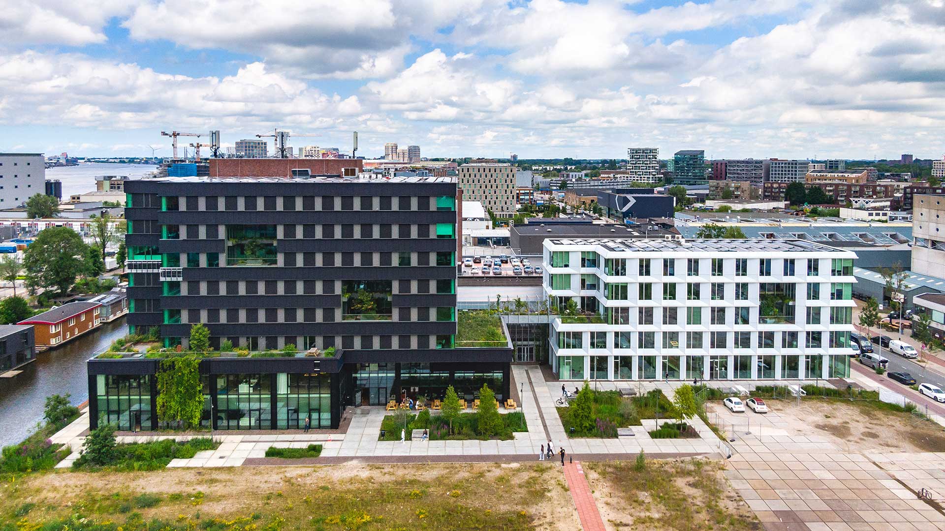 Aerial view of Max and Moore office buildings at Asterweg 13 in Amsterdam Noord, located along the water with green terraces, parking areas and surrounding urban landscape.