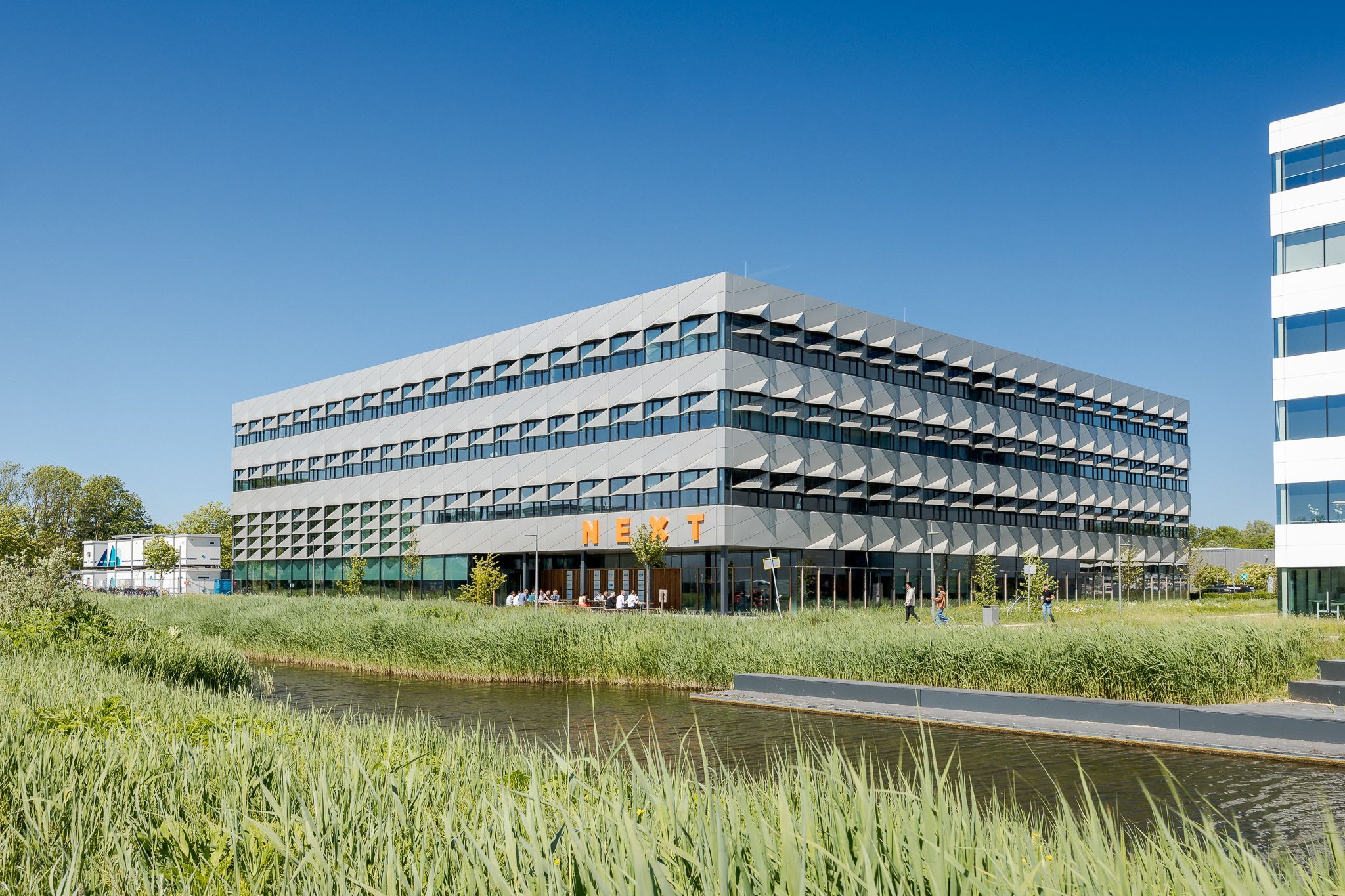 Nieuw en modern campus gebouw van de TU Delft met de letters 'NEXT' op het gevel.