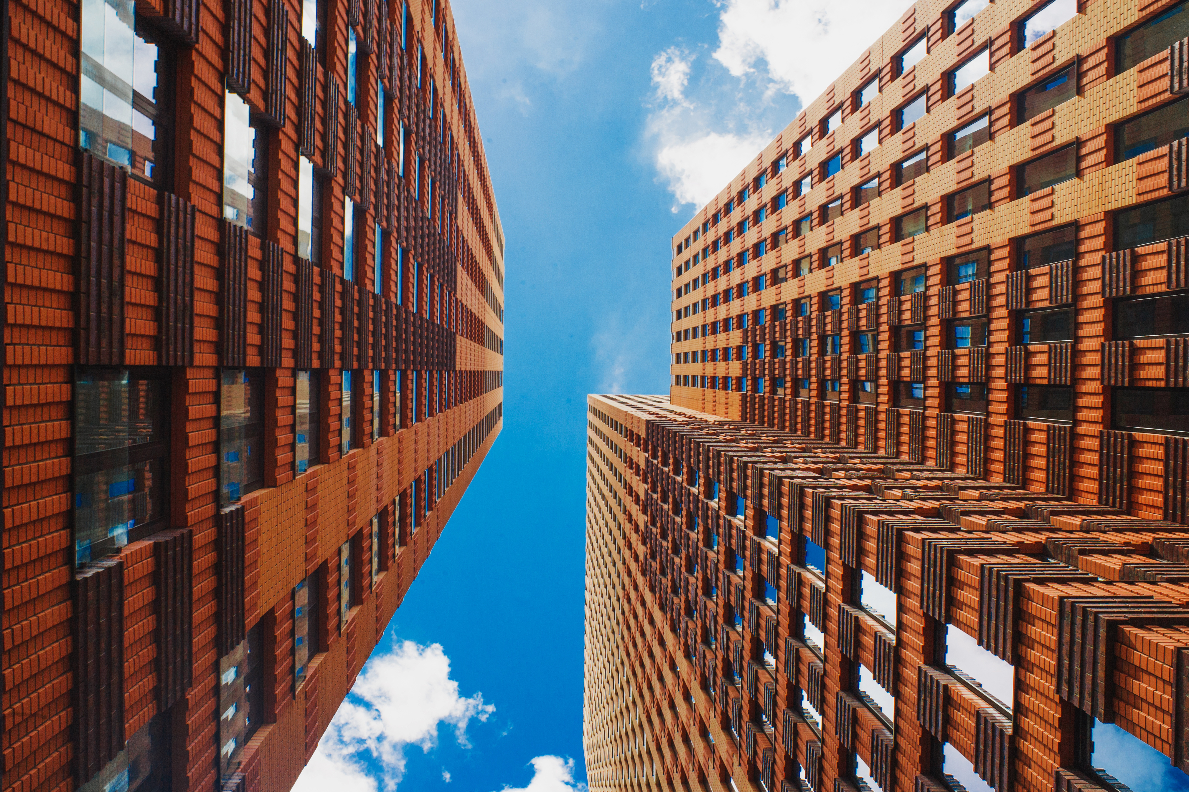 Low angle view between tall brick office buildings with distinctive facade patterns, large windows and a bright blue sky above urban architecture.