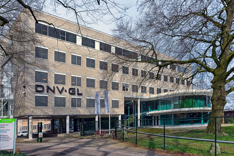 Kantoorgebouw met grote ramen en de tekst ‘DNV GL’ op de gevel. Het gebouw is omringd door grote bomen, een nette stoep en een grasperkje.