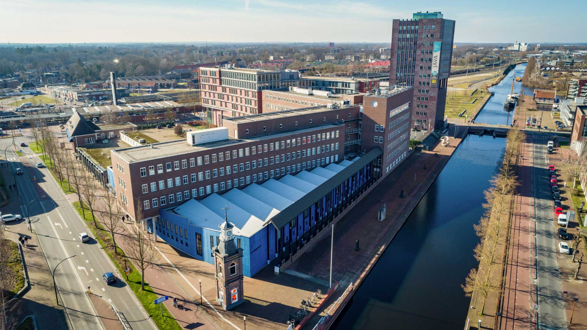 Luchtfoto van een stadslandschap met een kanaal omringd door gebouwen met gemengde architectuurstijlen onder een heldere hemel.