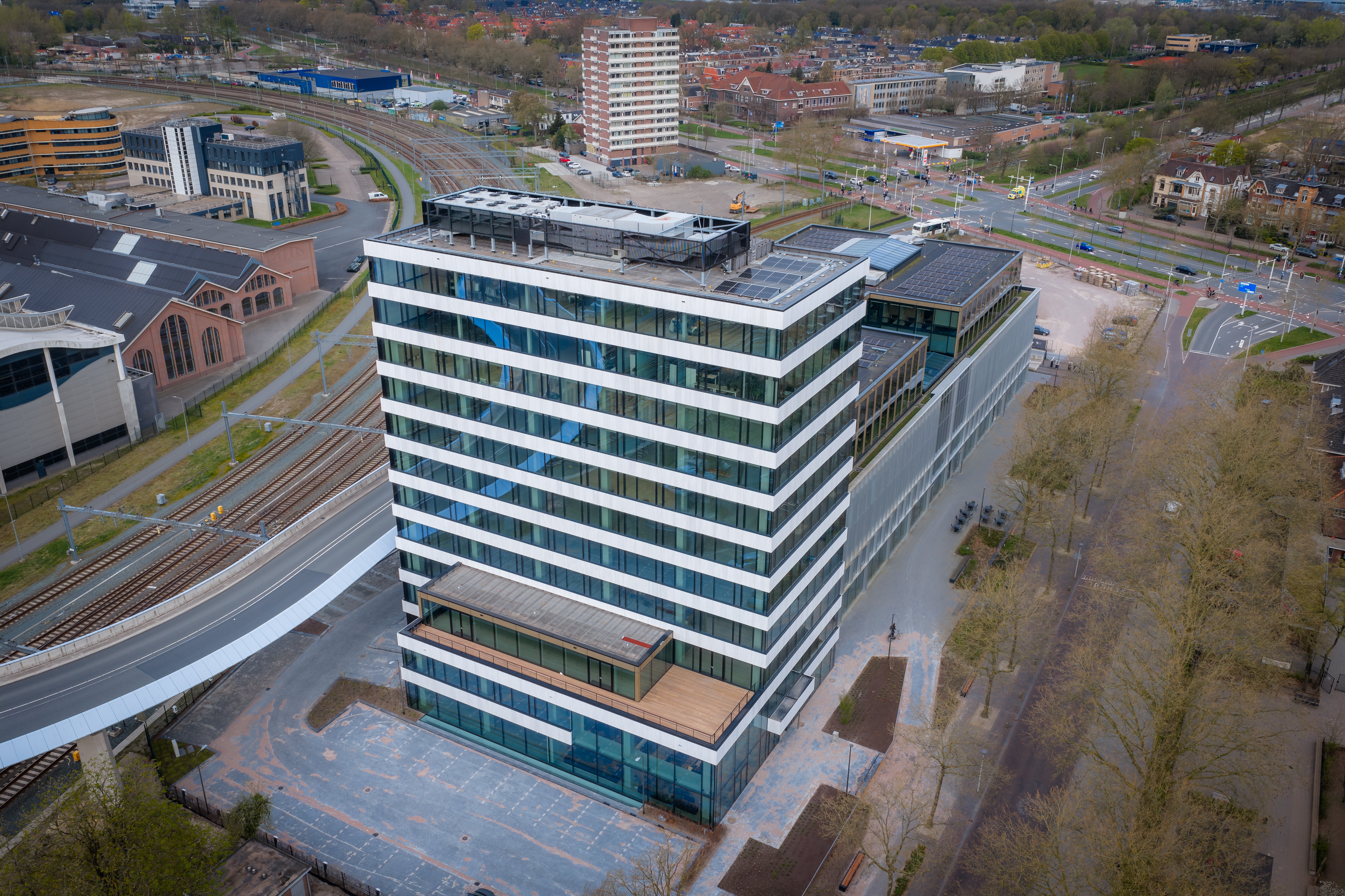 Luchtfoto van duurzaam kantoorgebouw City Post naast spoorlijnen en stationsgebied in Utrecht, met glazen gevels, zonnepanelen en stedelijke ontwikkeling.