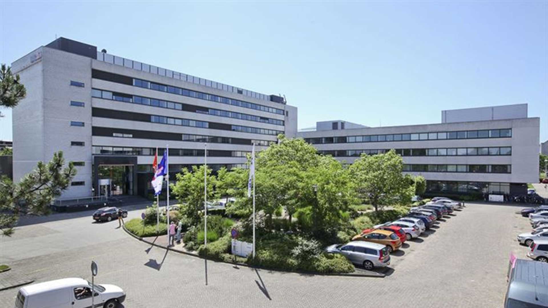 Modern kantoorgebouw met meerdere verdiepingen, omgeven door parkeerplaats en groen.