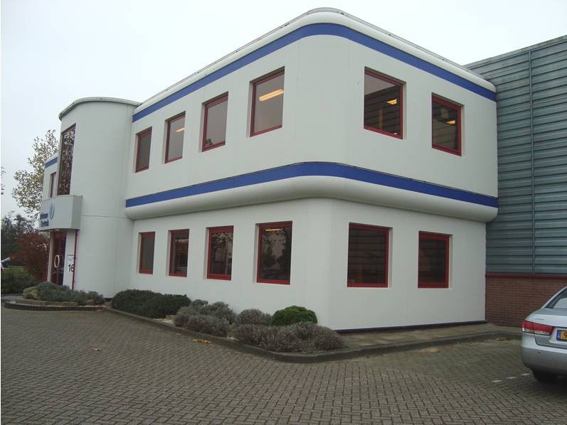 Een kantoorgebouw met twee etages die lijkt te zijn gevestigd op een industrie terrein. De witte gevel en de blauwe belijning geven het pand zijn kenmerkende uitstraling.