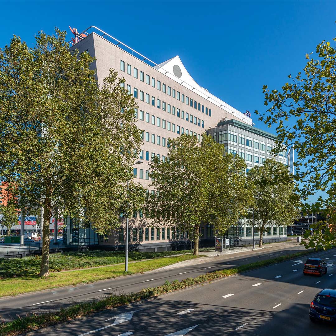 Een modern kantoorgebouw met een opvallende architectuur in Rotterdam, omgeven door bomen in de herfst.