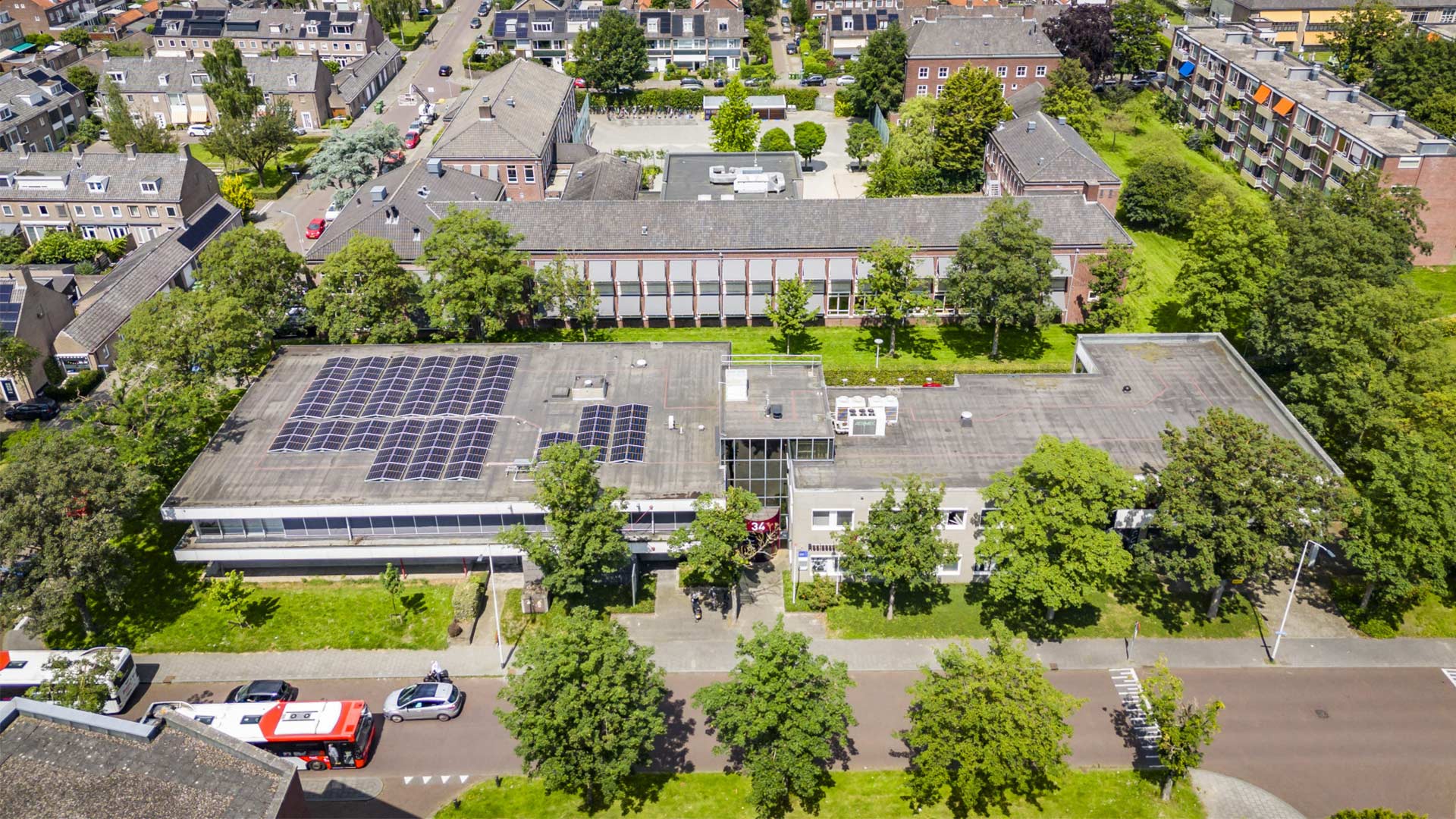 Een modern kantoorgebouw met een opvallende glazen gevel en gebogen vorm, omgeven door een parkeerplaats en andere gebouwen in een stedelijke omgeving.