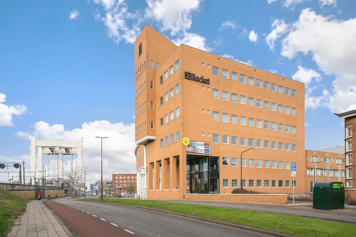 Een buitenstedelijke omgeving met een kantoorgebouw met orange bakstenen en met verschillende bedrijfsnamen op de gevel.