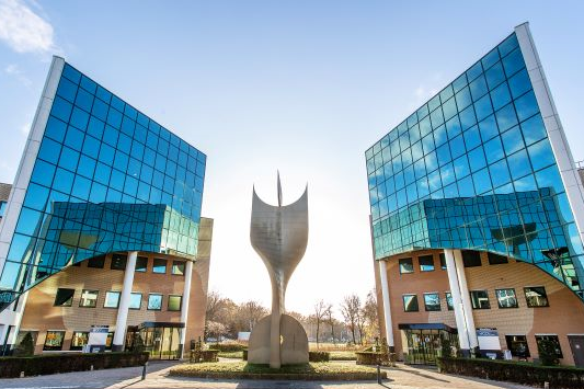 Exterior of two office buildings with reflective windows. A large sculpture stands in the open-plan office between the office buildings.