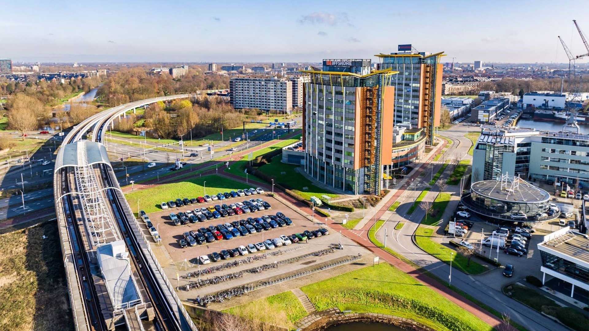 Een kantoorgebouw met daarnaast een parkeerplaats en treinstation.