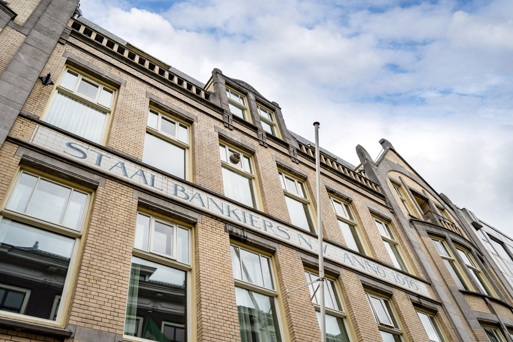 Gevel van een gebouw in klassieke architectuurstijl met ‘STAAIJ BANKIERS’ erop geschreven onder een bewolkte lucht.
