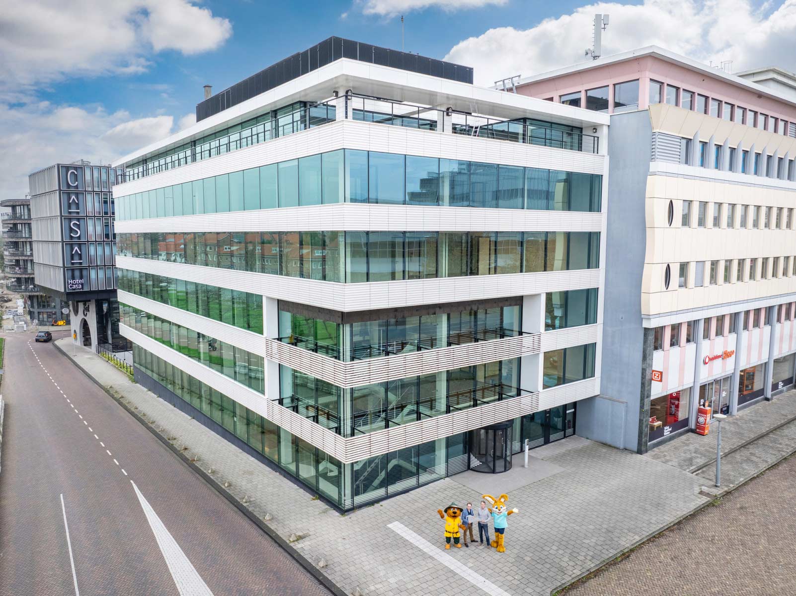 Een modern kantoorgebouw met een glazen gevel en opvallende architectuur, met enkele personen in kostuums voor het gebouw.